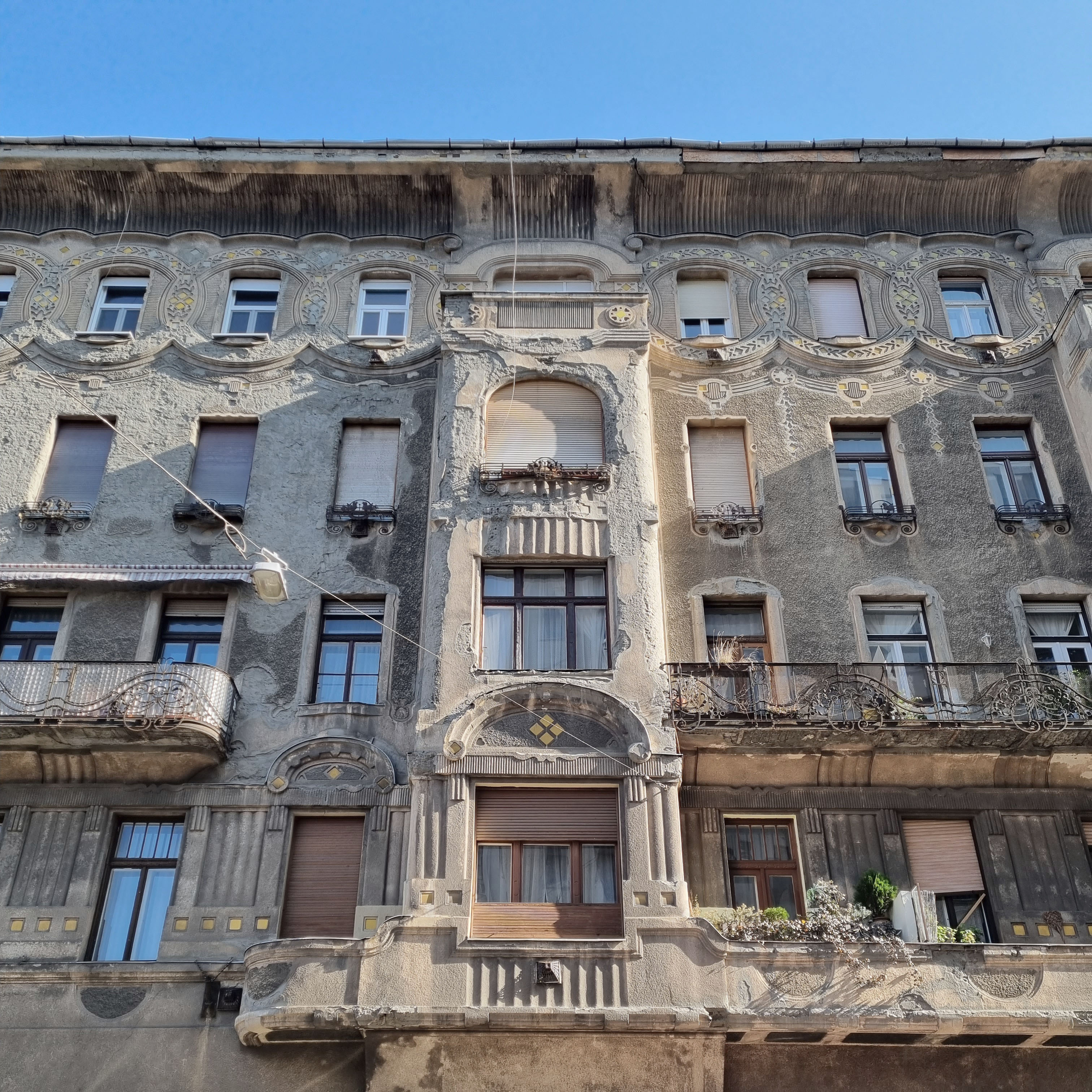 Visegrádi 17 façade before restoration, exposed brick patches and faded Art Nouveau curves, photo